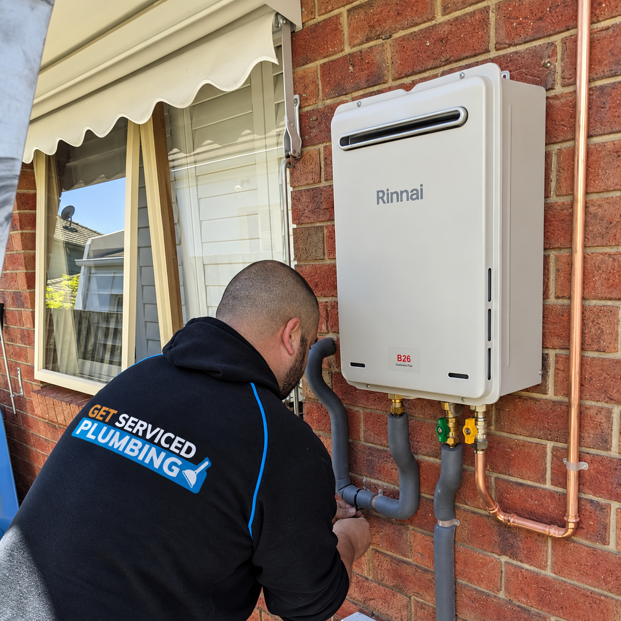 Oakleigh plumber 239 Dennis servicing a Rinnai continuous-flow hot water system on a brick wall